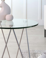 Round glass-top table with chrome-finished crisscross legs in a minimalist design.