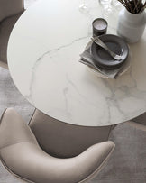 Round white marble-top dining table with a tapered cylindrical base, paired with a contemporary grey upholstered dining chair with a curved backrest.