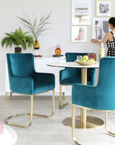 Elegant dining set featuring a round white table with a golden base, flanked by four luxurious teal velvet chairs with smoothly curved backrests and sleek gold metal legs.