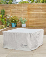 Outdoor furniture covered with a large, light grey protective cover bearing the logo of "Danetti Garden" on an outdoor wooden deck with potted plants nearby. The specific furniture underneath the cover is not visible.