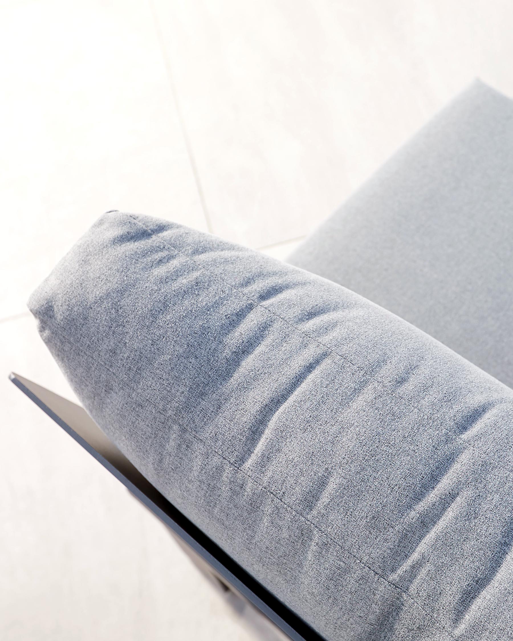 Close-up of a modern minimalist style sofa with a light grey fabric upholstery and a sleek black metal leg visible, set against a plain bright background.