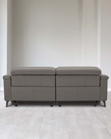 Modern two-piece sectional sofa with a simplistic design, featuring clean lines, in a muted grey upholstery. Each section showcases a smooth back and seat with no visible cushions, raised on low-profile dark wooden legs. The sofa is positioned against a plain wall on light wooden flooring.