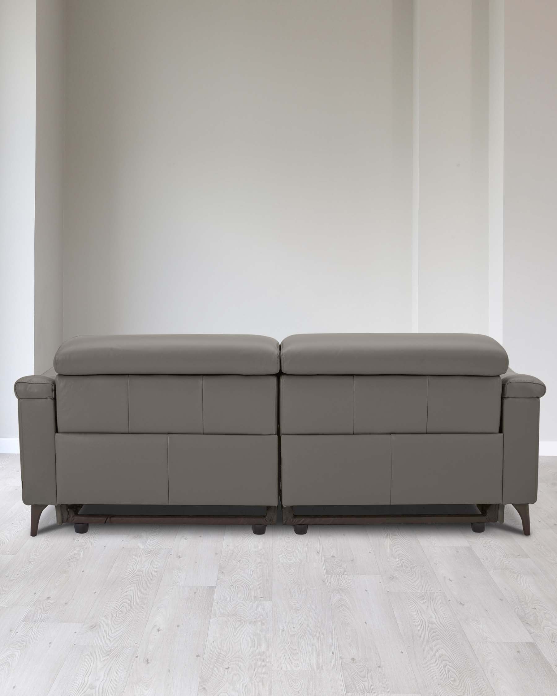 Modern two-piece sectional sofa with a simplistic design, featuring clean lines, in a muted grey upholstery. Each section showcases a smooth back and seat with no visible cushions, raised on low-profile dark wooden legs. The sofa is positioned against a plain wall on light wooden flooring.