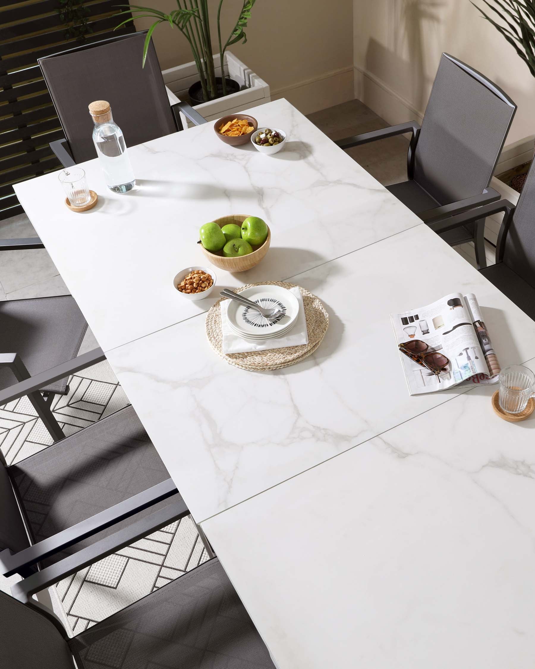 Modern dining set featuring a rectangular white marble tabletop with dark grey metal legs, complemented by four sleek, armless dining chairs with dark grey fabric seats and backrests mounted on matching dark grey metal frames. The setting is accented with simple tableware and decorative items.