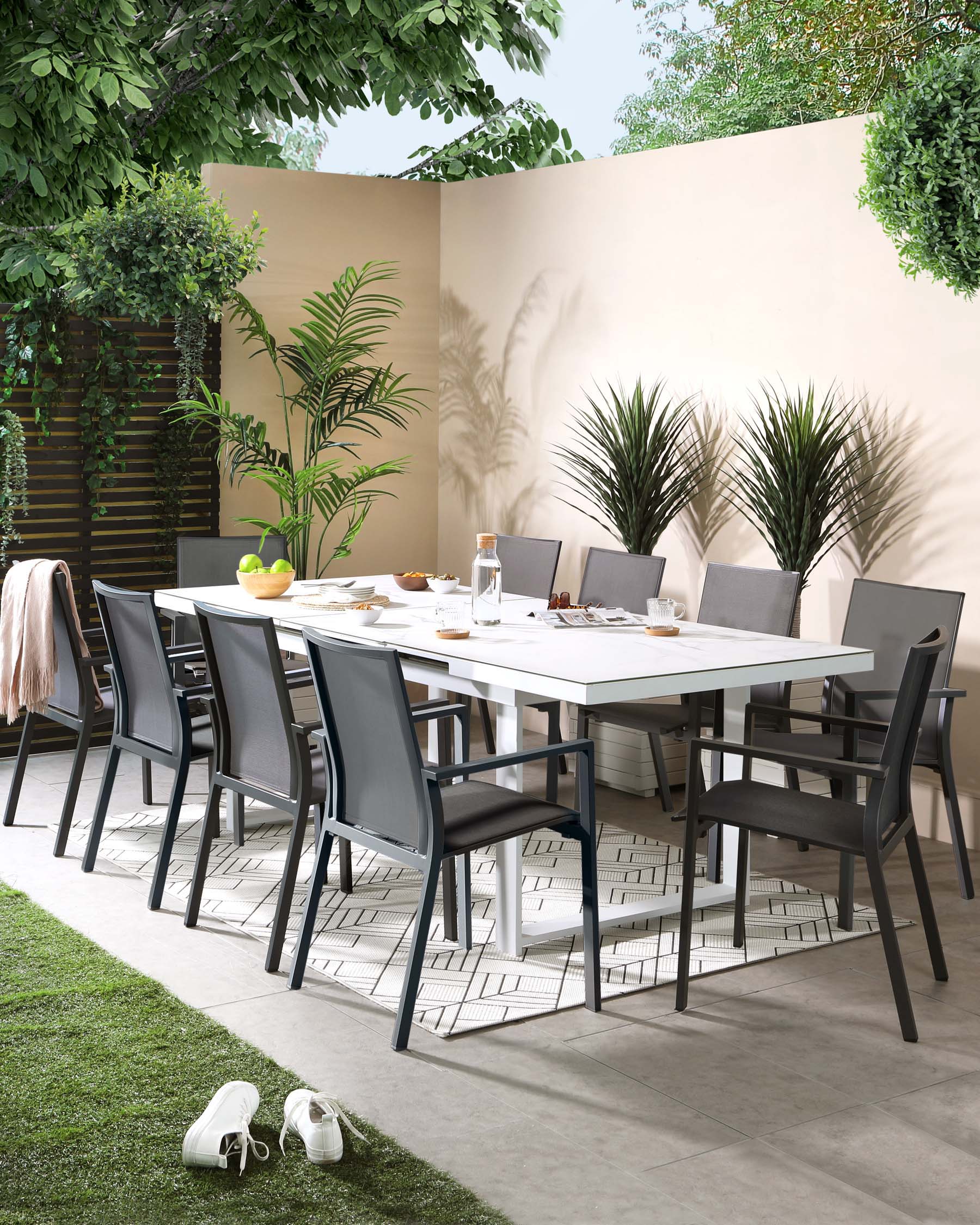 Modern outdoor dining furniture set including a rectangular white tabletop with a smooth finish and dark grey straight legs, paired with six sleek armchairs featuring dark grey frames and matching textilene fabric for comfortable seating. The set is presented on a patio with tile flooring, surrounded by green plants, suggesting a stylish and functional design for al fresco dining.