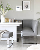 Modern minimalist furniture set featuring a sleek white desk with a glossy finish paired with a contemporary grey leather chair that has a curved backrest and shiny chrome sled legs. Completing the set is a matching grey leather ottoman with a simple cube design and a similar chrome base, which hosts a soft beige throw blanket on top. The furniture ensemble displays a harmonious blend of functionality and sophisticated design, perfect for a chic office space.