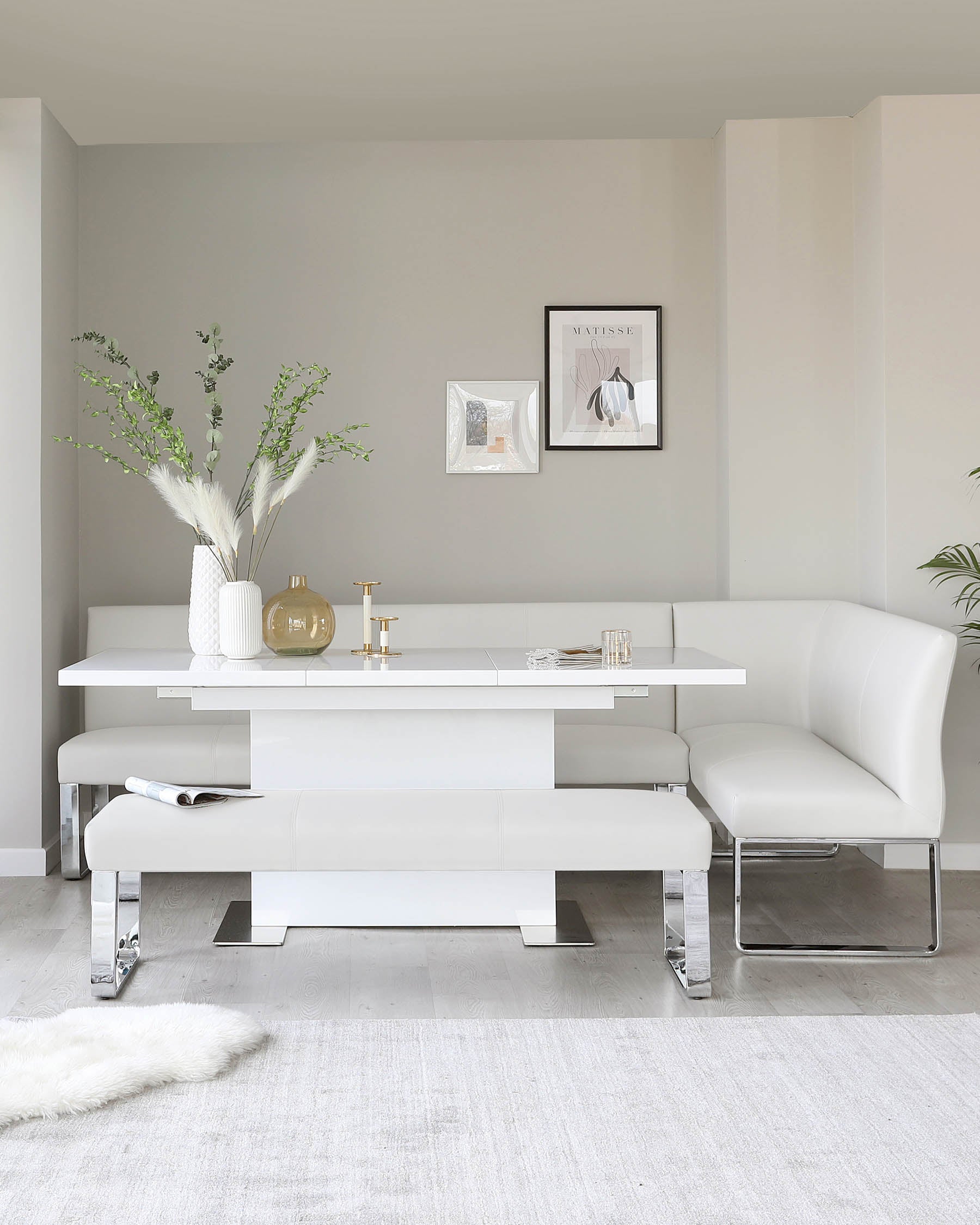 Modern white dining set featuring a sleek table, corner bench, and minimalist seating, accented with stylish decor.