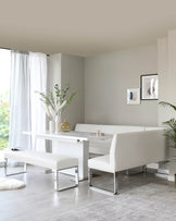 Modern white dining set featuring a rectangular table, sleek bench, and curved seating, complemented by light decor.