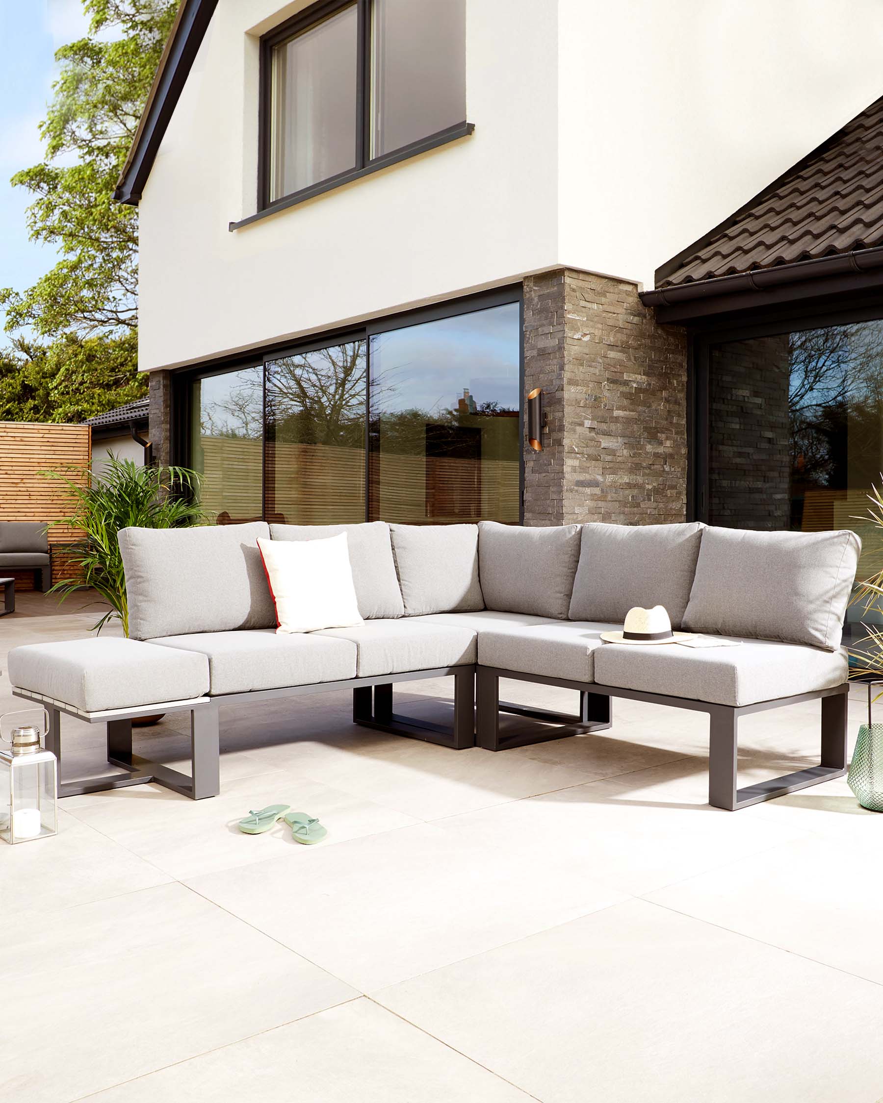 Modern outdoor sectional sofa with light grey cushions on a sleek, dark metal frame, featuring an L-shaped design with an attached square ottoman. Decorative pillows included.