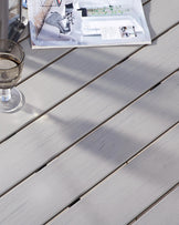 Sleek, modern outdoor table with light grey wooden slats on the surface, bathed in sunlight.