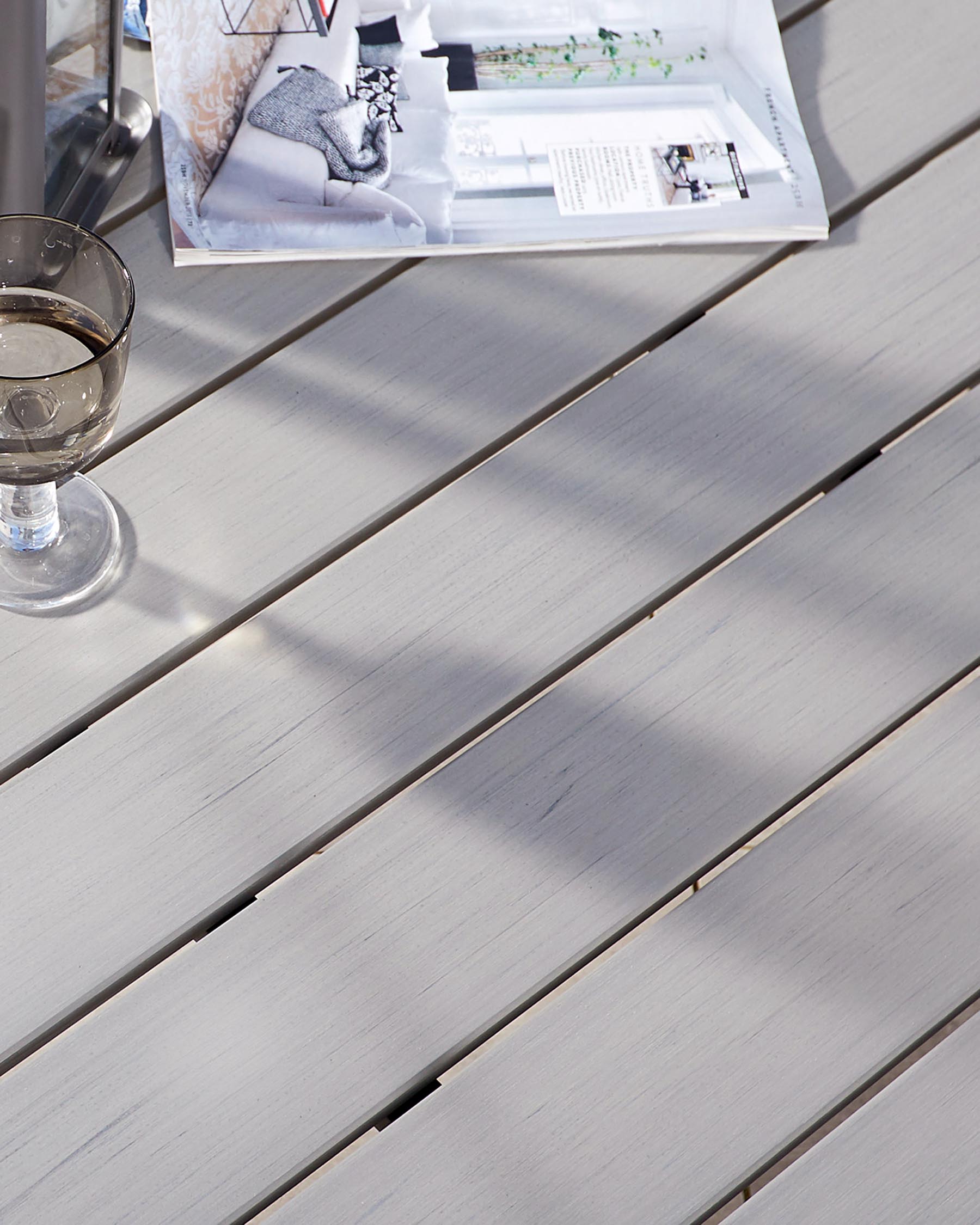 Sleek, modern outdoor table with light grey wooden slats on the surface, bathed in sunlight.