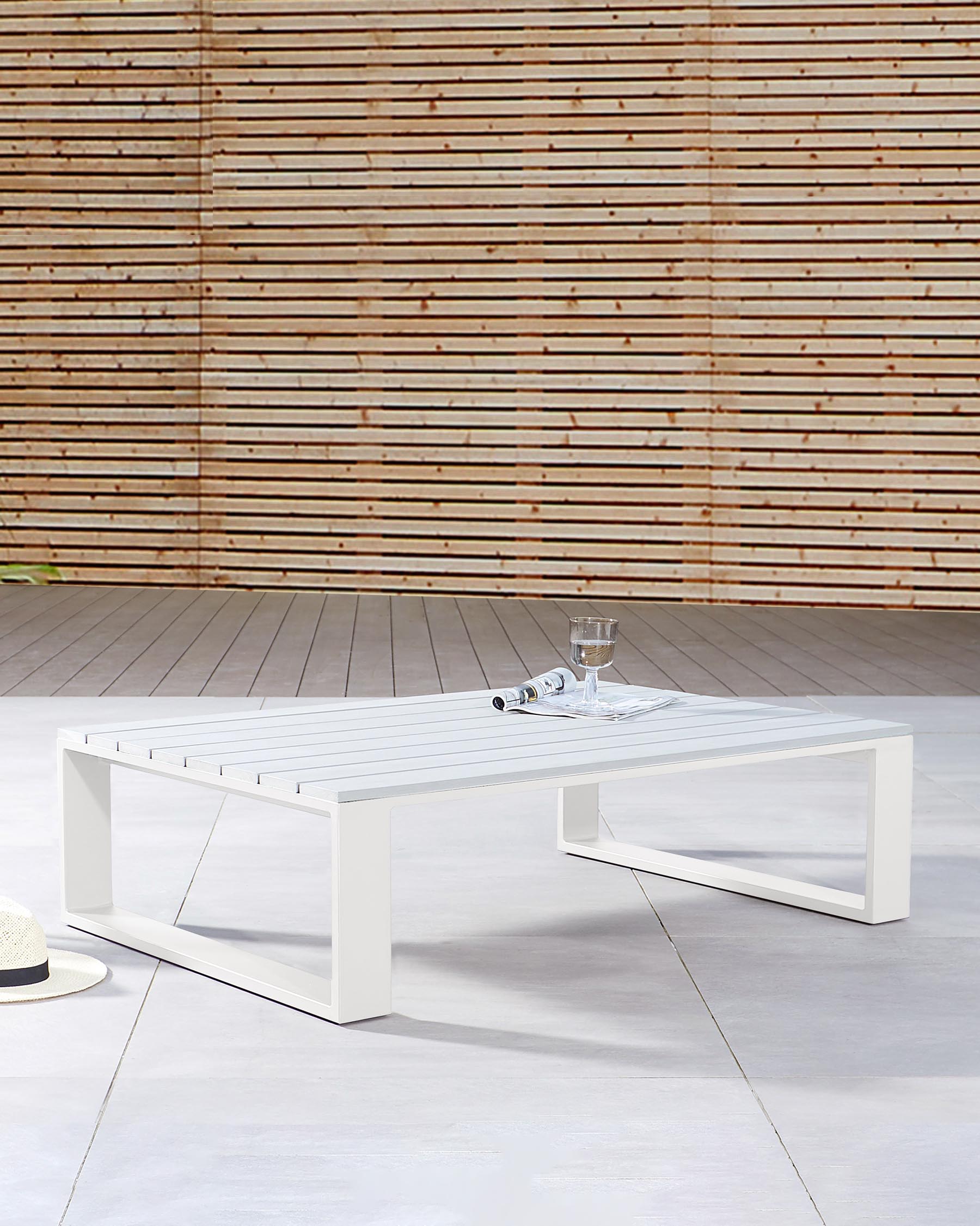 Modern outdoor white rectangular coffee table with a minimalistic design, featuring clean lines and a slatted top, set on a patio with a wooden slat background.