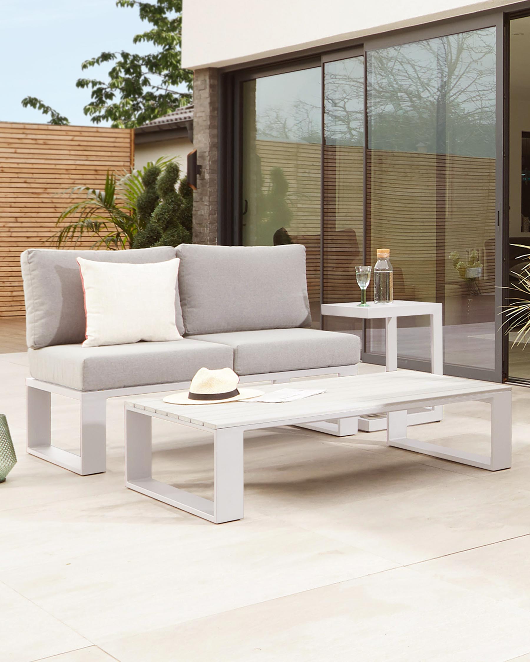 Modern outdoor furniture set featuring a two-seater sofa with grey cushions and additional throw pillows, paired with a low-profile, white rectangular coffee table, showcased on a patio setting.