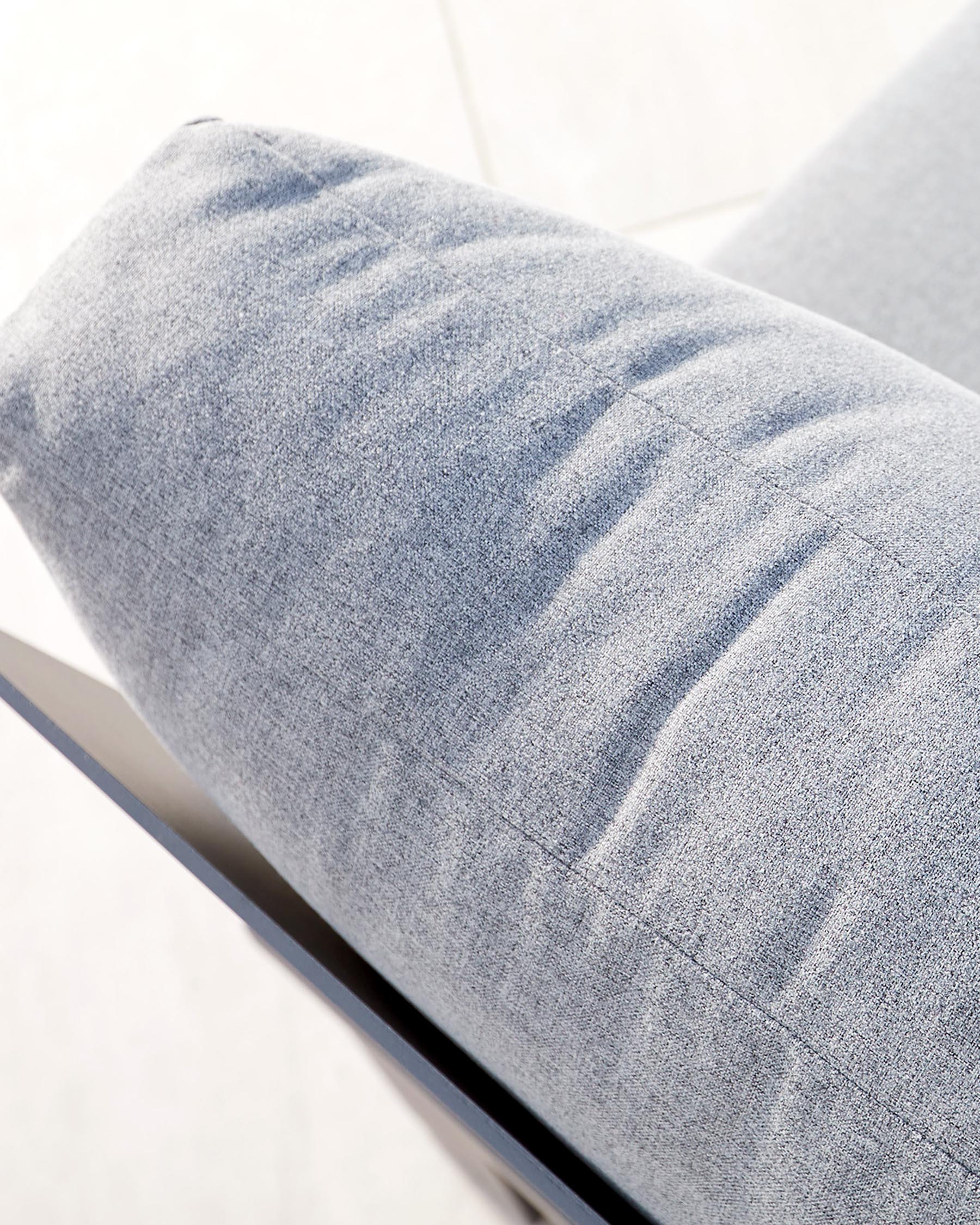 Close-up of a light grey upholstered cushion with a textured fabric, possibly part of a modern outdoor furniture set, showcasing subtle shadow lines and stitching details with a minimalist metallic frame visible at the bottom edge.