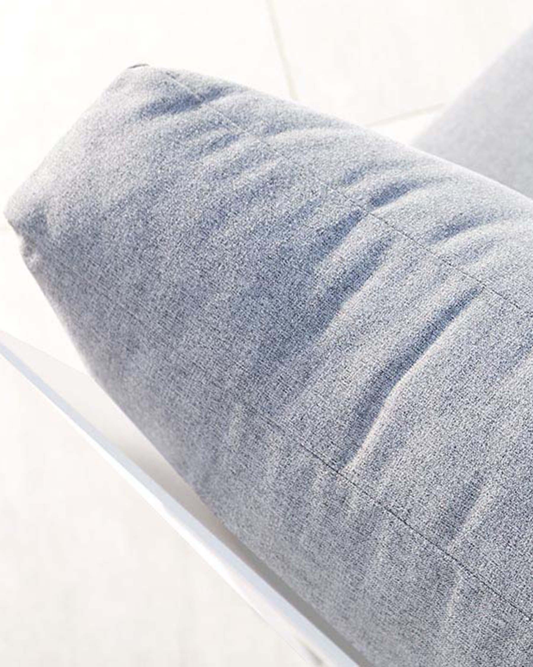 Close-up of a light grey upholstered cushion with a textured fabric, possibly part of a modern sofa or chair, set against a pale background.