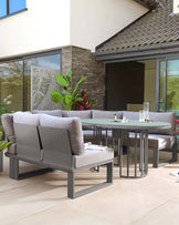 Modern outdoor furniture set including a grey sectional sofa with plush cushions and two minimalist black circular side tables, complemented by a matching grey round dining table with a glass top and a built-in lazy Susan.