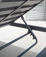 Close-up view of a modern outdoor chaise lounge with a matte black aluminium frame and grey sling fabric, highlighting its sleek design and sturdy construction.