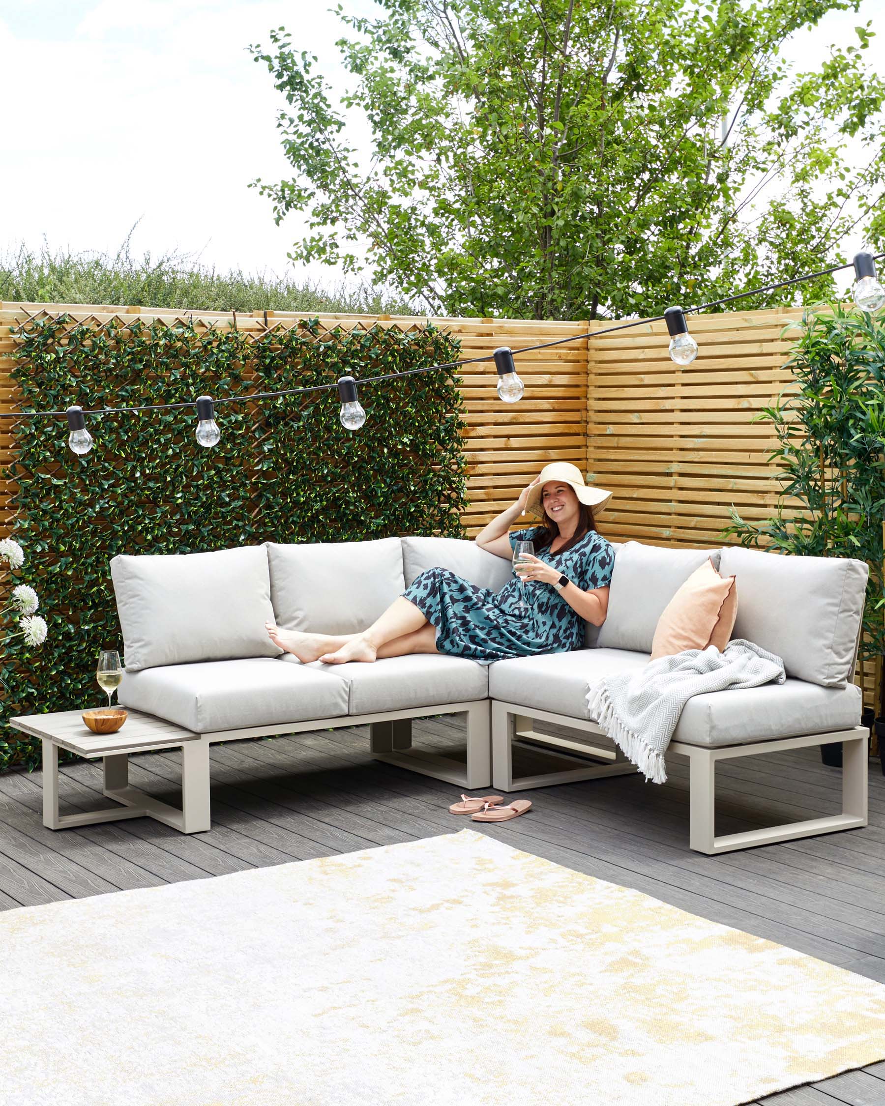 Contemporary outdoor sectional sofa with light grey cushions on a white aluminium frame, paired with a matching low-profile rectangular coffee table, set upon a large cream and beige patterned area rug.