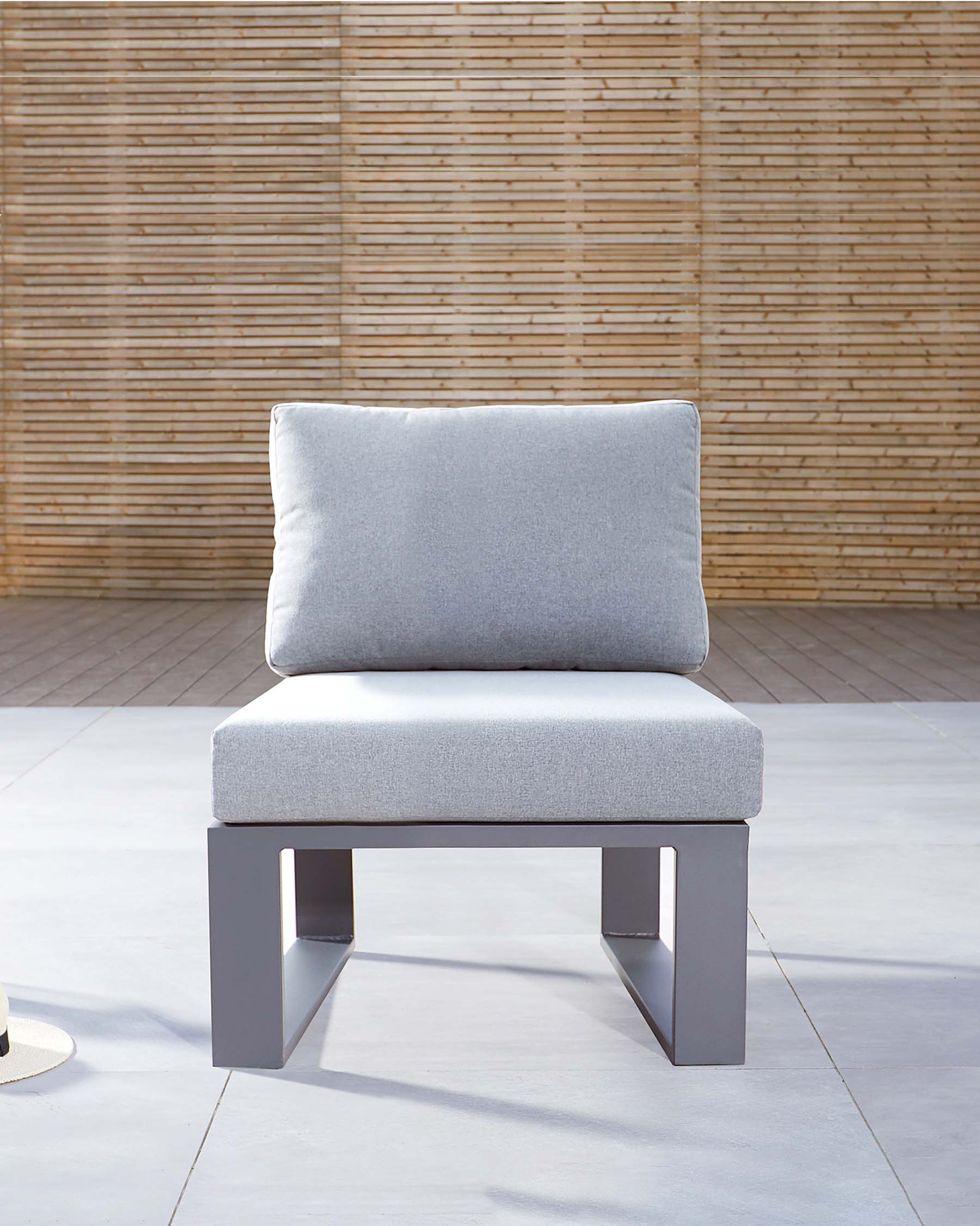 Modern minimalist outdoor chair with a sleek grey metal frame and light grey cushioned seat and backrest, set against a bamboo wall backdrop.