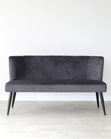 Modern charcoal grey sofa with a textured chevron pattern on the backrest and a smooth seat, supported by four black tapered legs. Positioned against a white wall on light wooden flooring.