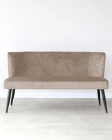 A modern taupe upholstered loveseat with a unique chevron pattern on the backrest and seat, featuring sleek angled wooden legs in a dark finish.