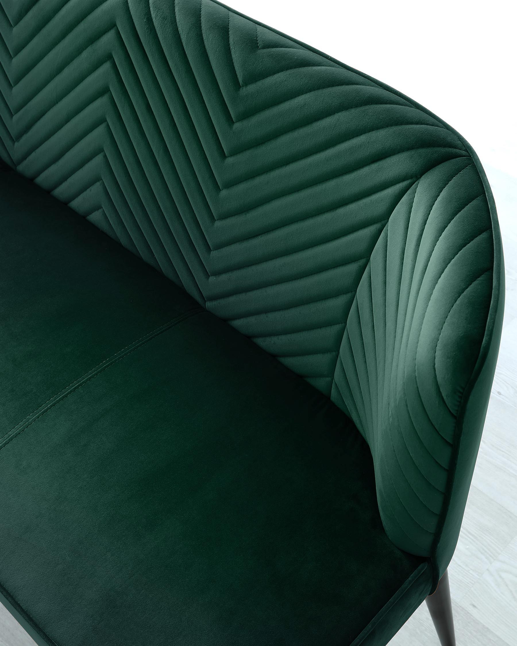 Luxurious dark green velvet sofa with pleated backrest and curved arm detailing, showcasing a sophisticated blend of comfort and stylish design.