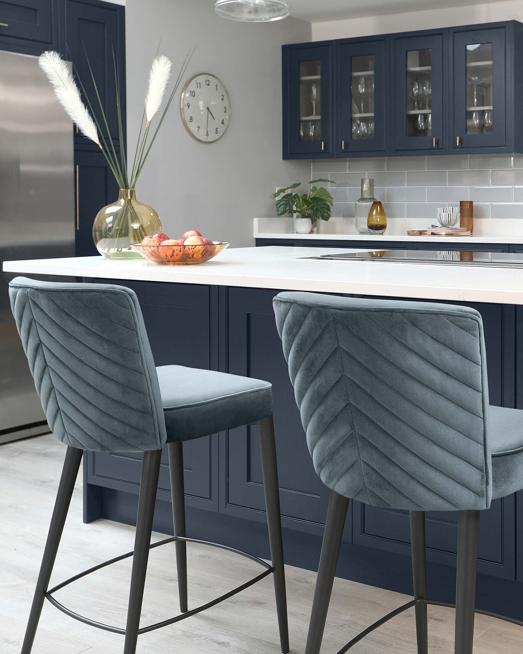 Two elegant grey upholstered barstools with chevron patterned backs and sleek metal legs in front of a modern kitchen island with a white countertop.