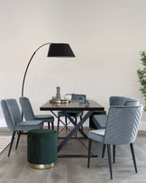 A modern dining set featuring a rectangular table, plush velvet chairs with quilted backs, a round stool, and a stylish floor lamp.