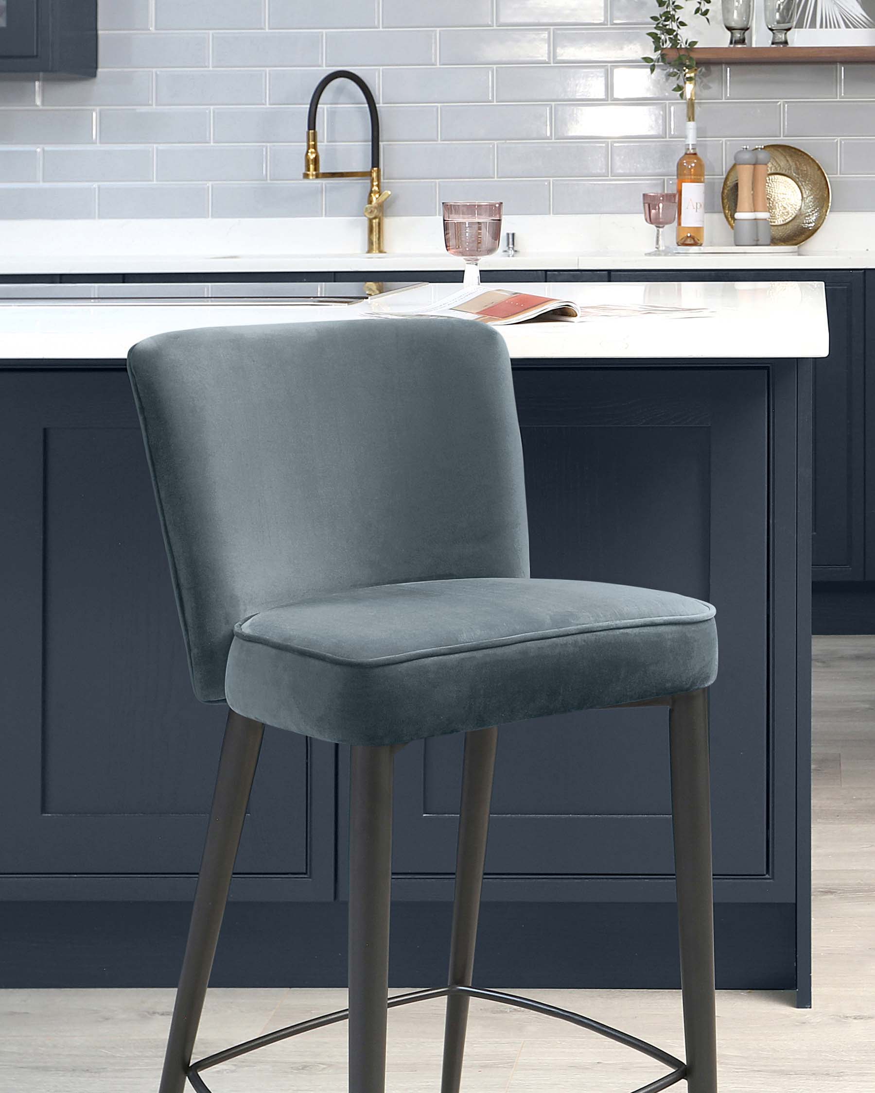 Elegant modern bar stool with a smooth grey velvet seat and sleek metal legs in a matte black finish, featuring a comfortable curved backrest and a footrest for added support.