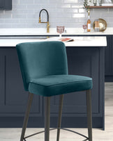 Elegant teal upholstered bar stool with a high back and slim metal legs in a dark finish, positioned against a kitchen island.