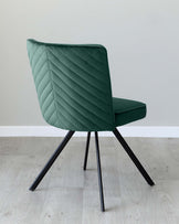 Modern teal upholstered chair with quilted backrest and angled black metal legs on a light wood flooring against a grey wall.