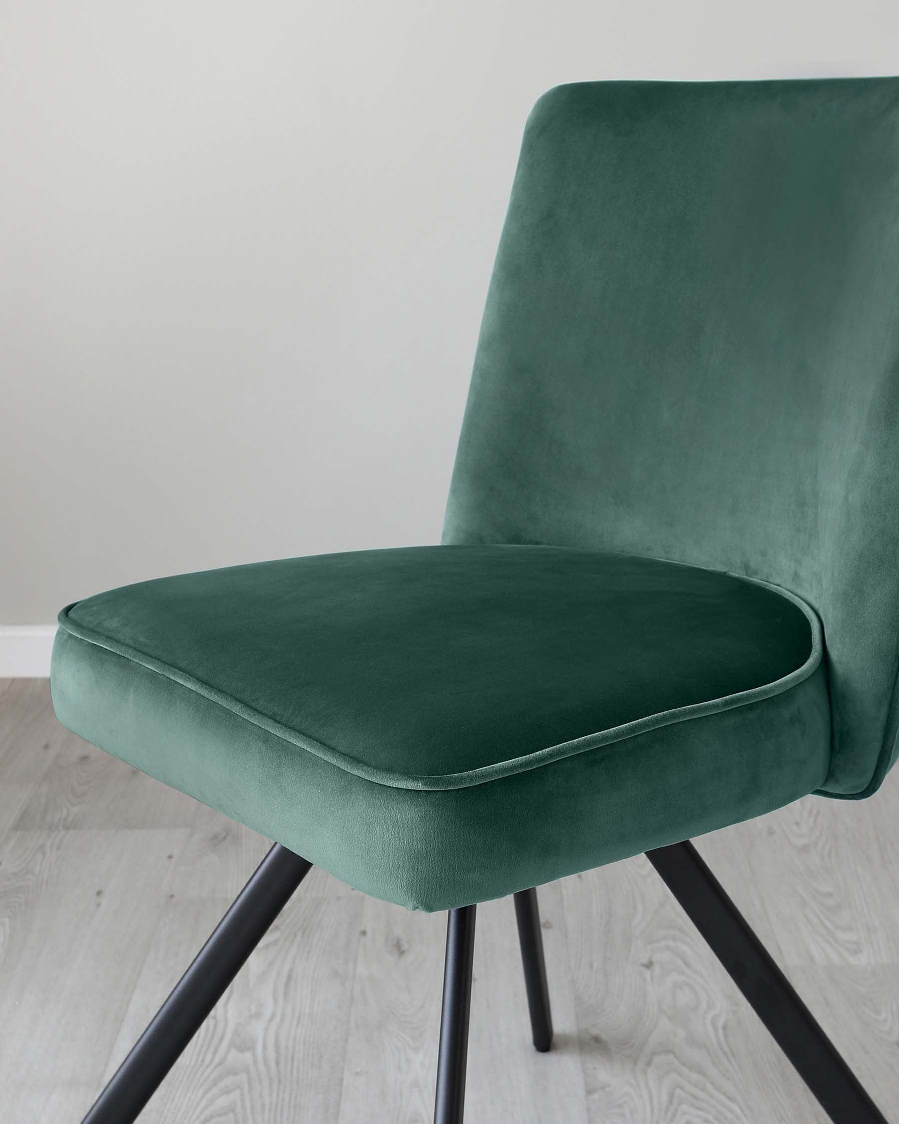 An elegant modern dining chair with plush emerald green velvet upholstery and a high backrest. This chair features a comfortable, cushioned seat and sits on sleek, angled black metal legs. Its sophisticated design adds a touch of luxury to any contemporary interior.