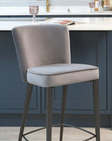 Elegant modern bar stool with a grey velvet upholstered seat and high backrest, featuring slender metal legs in a matte black finish, with a simple footrest design.