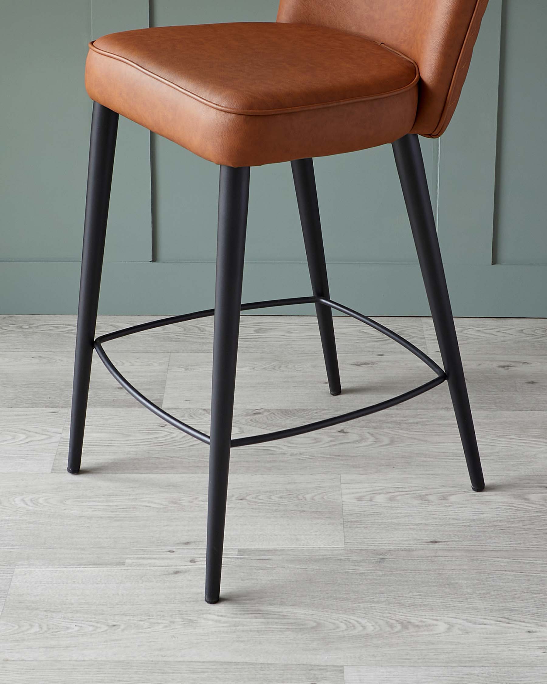 Modern barstool with tan faux leather cushioned seat and backrest on a sturdy four-legged black metal frame with a circular footrest.