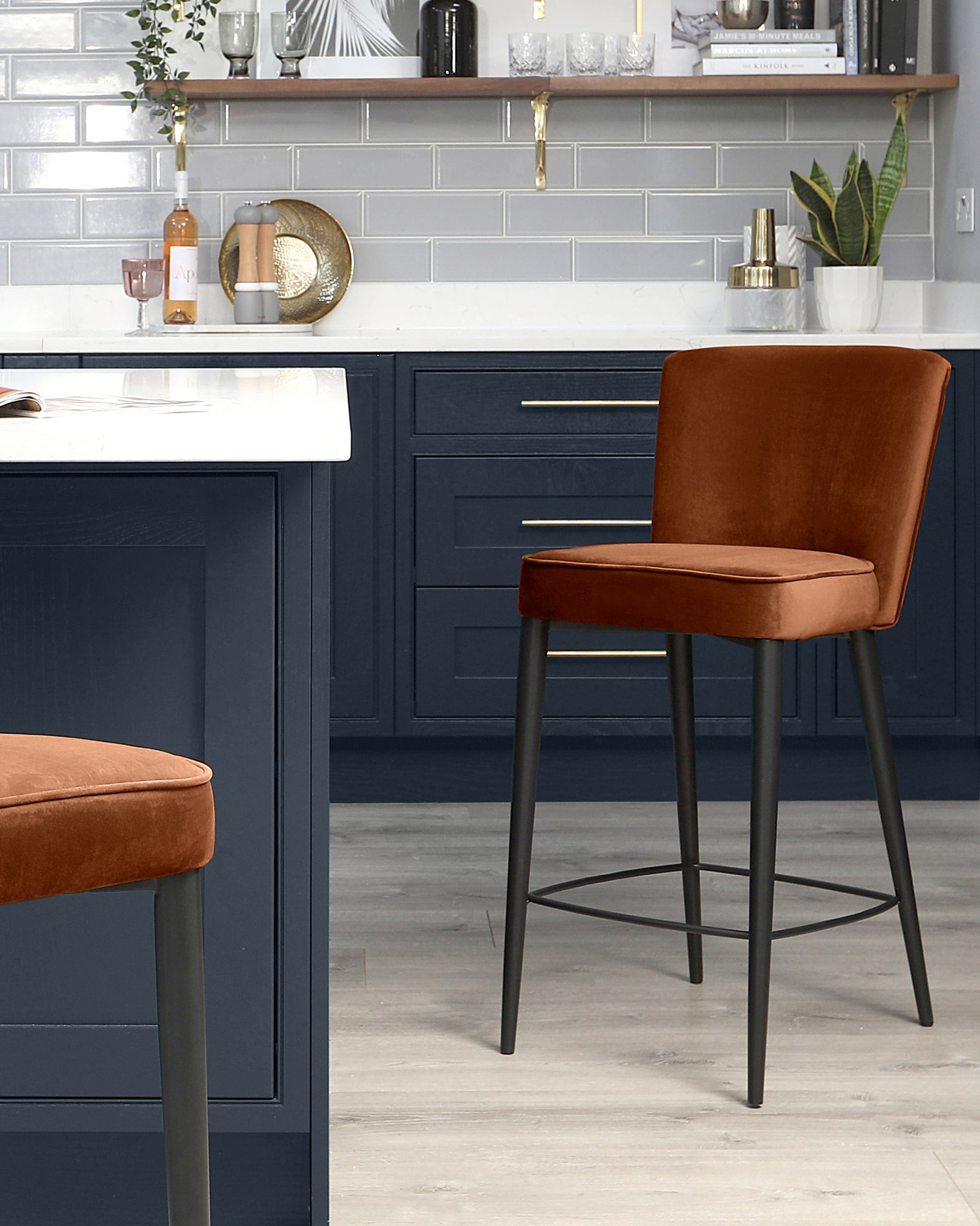 Modern kitchen bar stools with rust-coloured velvet upholstery and matte black metal legs.