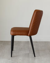 Modern minimalist chair with a sleek design, featuring a tan faux leather upholstery with quilted backrest detailing, and contrasting black metal legs.