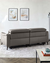 Elegant modern slate grey leather sofa with a minimalist design and clean lines, showcasing cushioned straight back and wide armrests, complemented by a low-profile white and grey patterned area rug, and a chic black-framed glass coffee table with a white marble effect top, positioned on a herringbone wooden floor.