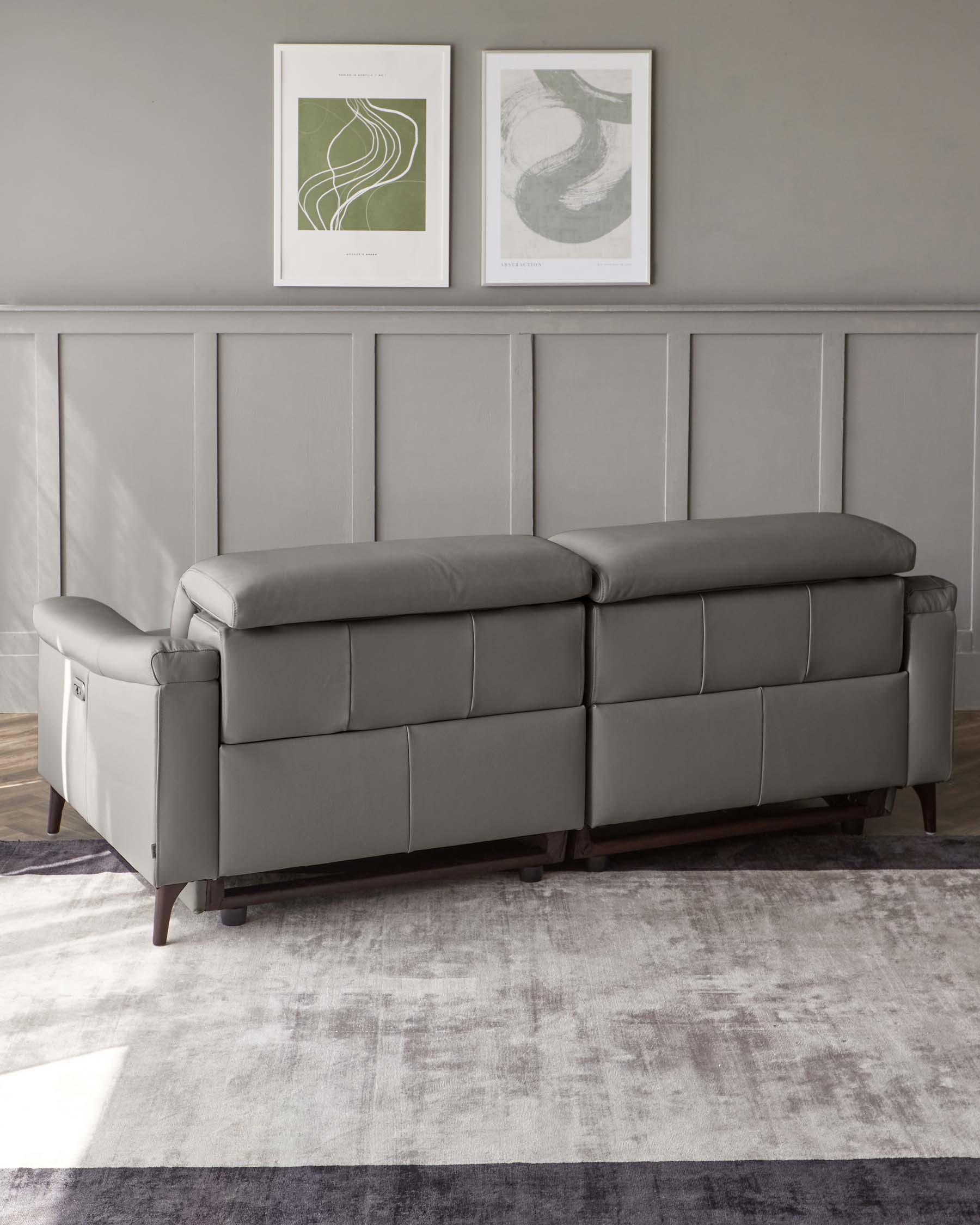 Elegant modern grey leather sofa with a smooth, streamlined design, featuring plush backrest cushions, padded armrests, and dark wooden legs.