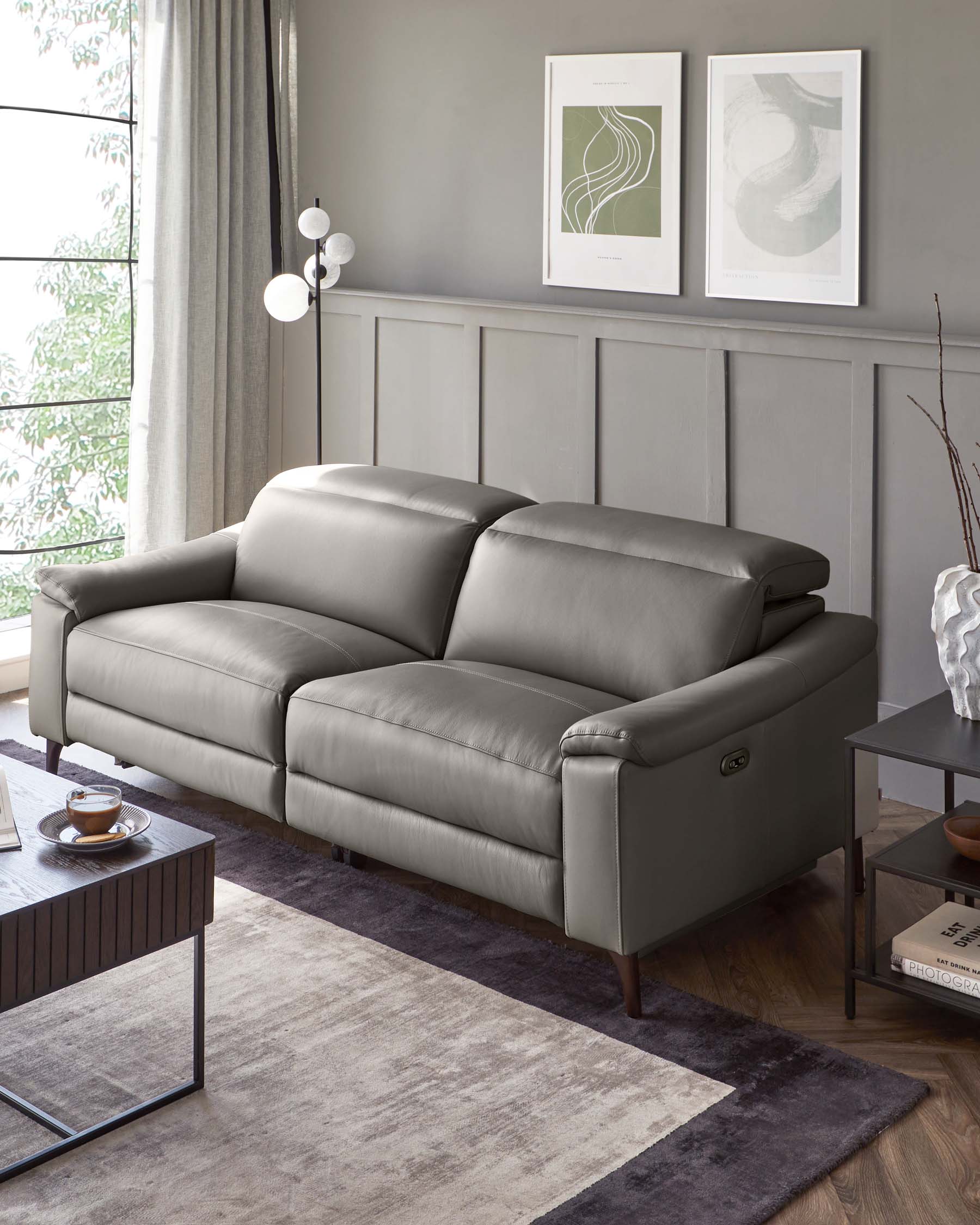 Modern grey leather sofa with cushioned armrests and recliner functionality, accompanied by a dark wood and metal frame coffee table with a clear glass top, set on a gradient grey area rug.