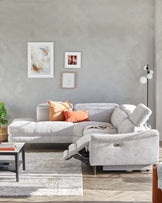 L-shaped grey fabric sectional sofa with recliner feature and adjustable headrests, complemented by a minimalist black coffee table with red and grey accents. A textured light rug under the coffee table enhances the living space.