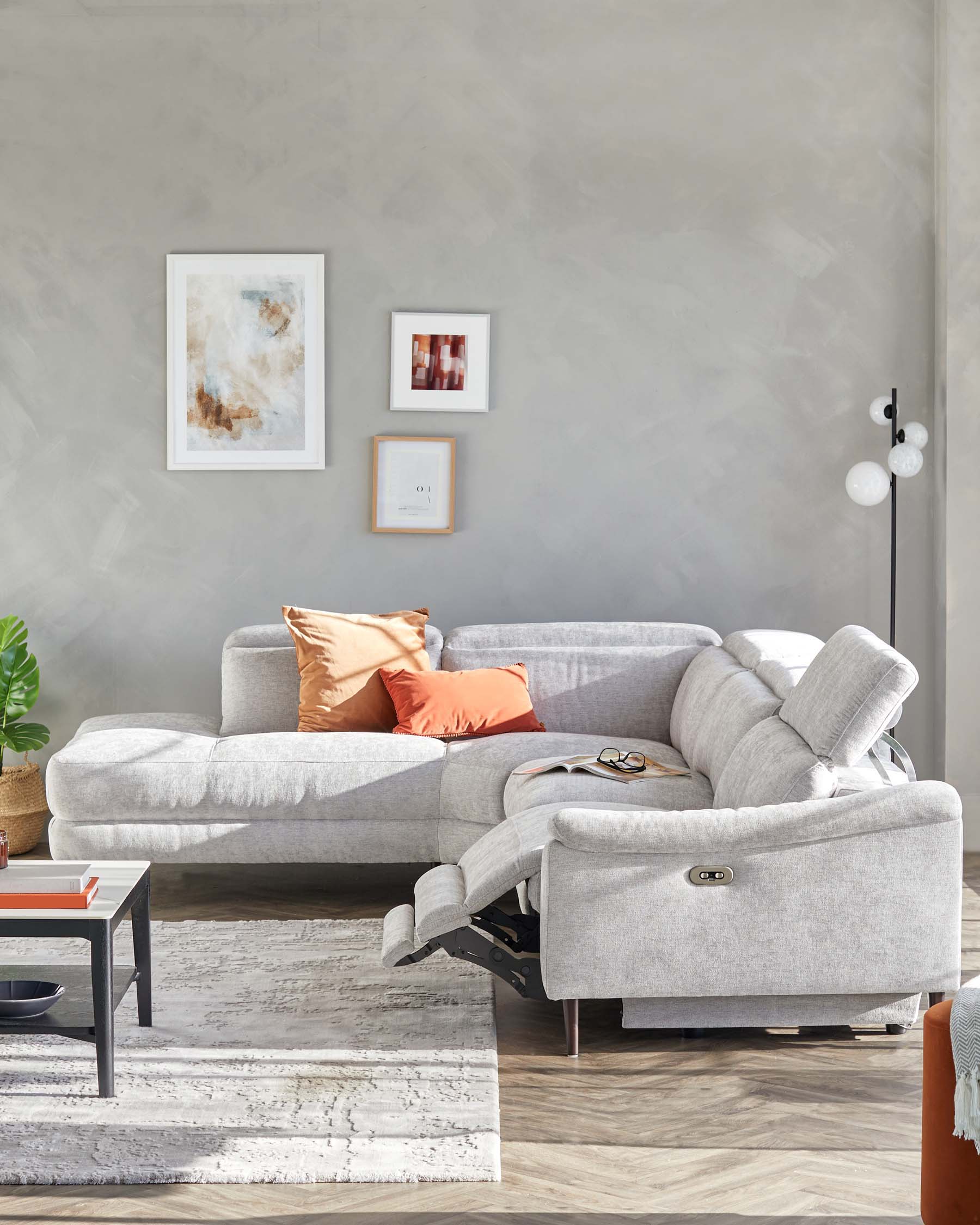 L-shaped grey fabric sectional sofa with recliner feature and adjustable headrests, complemented by a minimalist black coffee table with red and grey accents. A textured light rug under the coffee table enhances the living space.