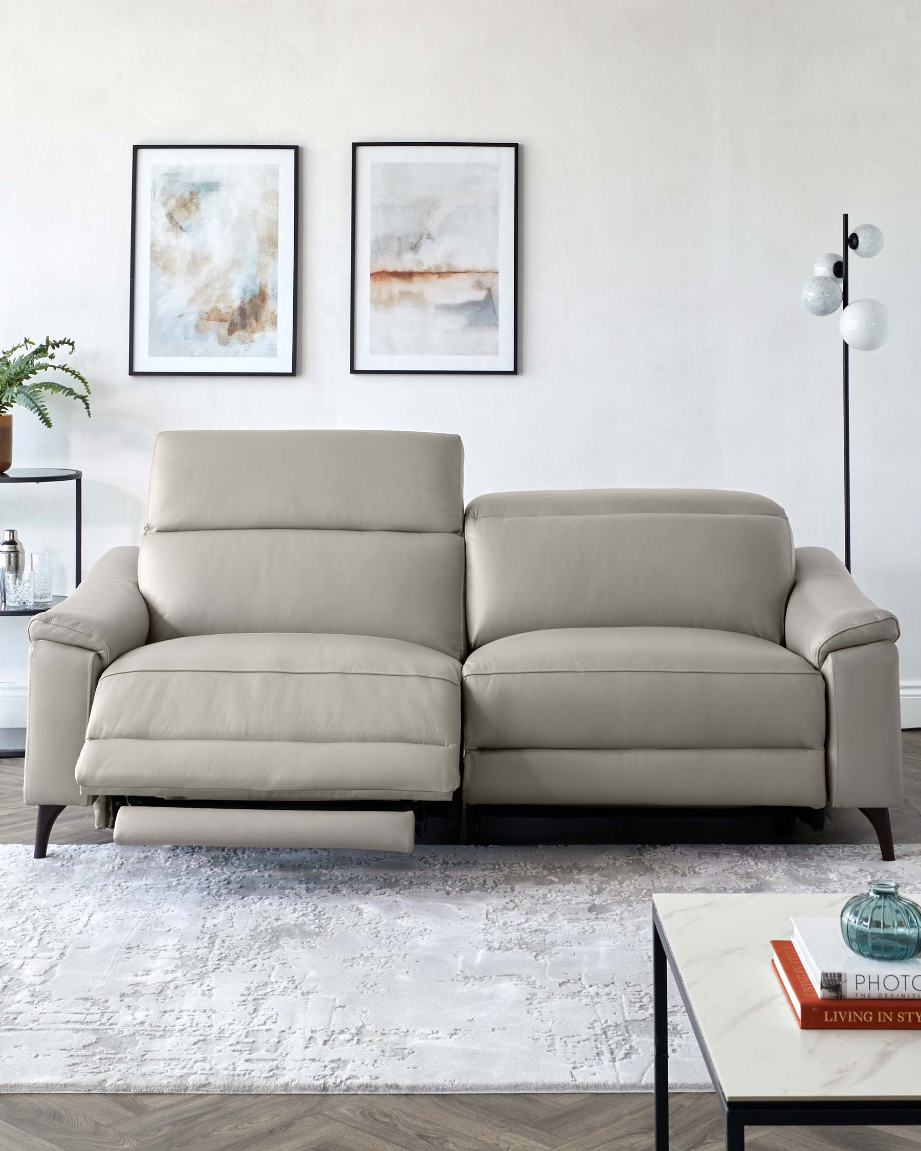 A sleek, light gray reclining sofa with plush cushions, paired with a modern coffee table and decorative art on the wall.