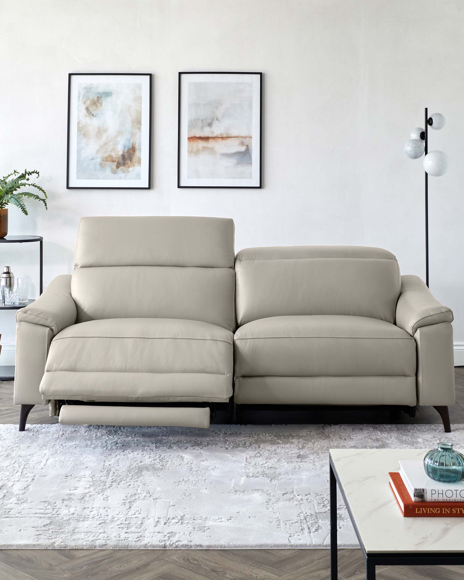 A modern, light gray leather reclining sofa with clean lines, complemented by a chic coffee table and abstract wall art.