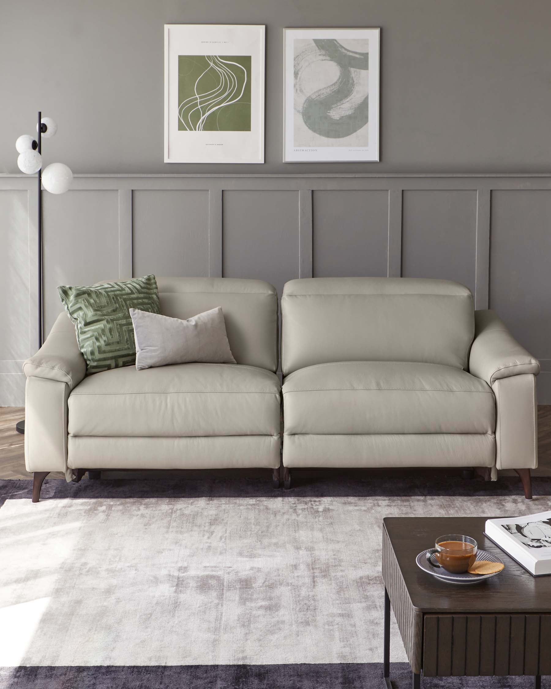 Elegant three-seater sofa in a neutral colour with plush upholstery and clean lines, paired with a minimalist dark wooden coffee table featuring a simple geometric design and a lower shelf. Set upon a contemporary faded area rug in a room with muted wall tones and subtle artwork.