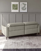 A modern, sleek light grey modular sofa with a tufted back, cushioned seats, and rounded armrests on dark wooden legs, displayed against a grey wall with wainscoting and framed abstract art pieces, positioned on a two-tone purple and grey area rug.