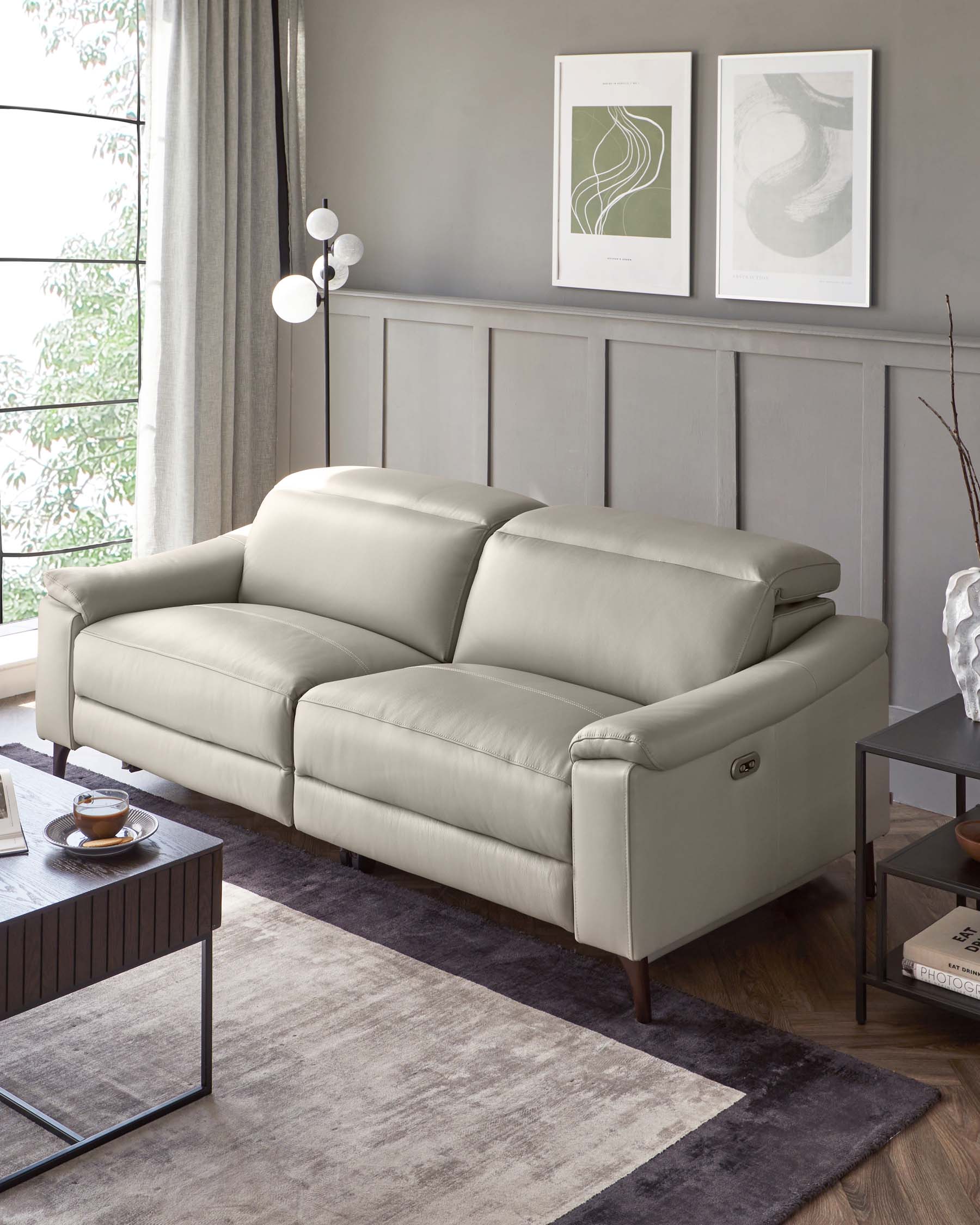 Contemporary light grey leather sofa with plush cushions and a sleek, minimalist design, featuring rounded armrests and dark wooden legs, showcased in a modern living room setting with coordinating decor elements.