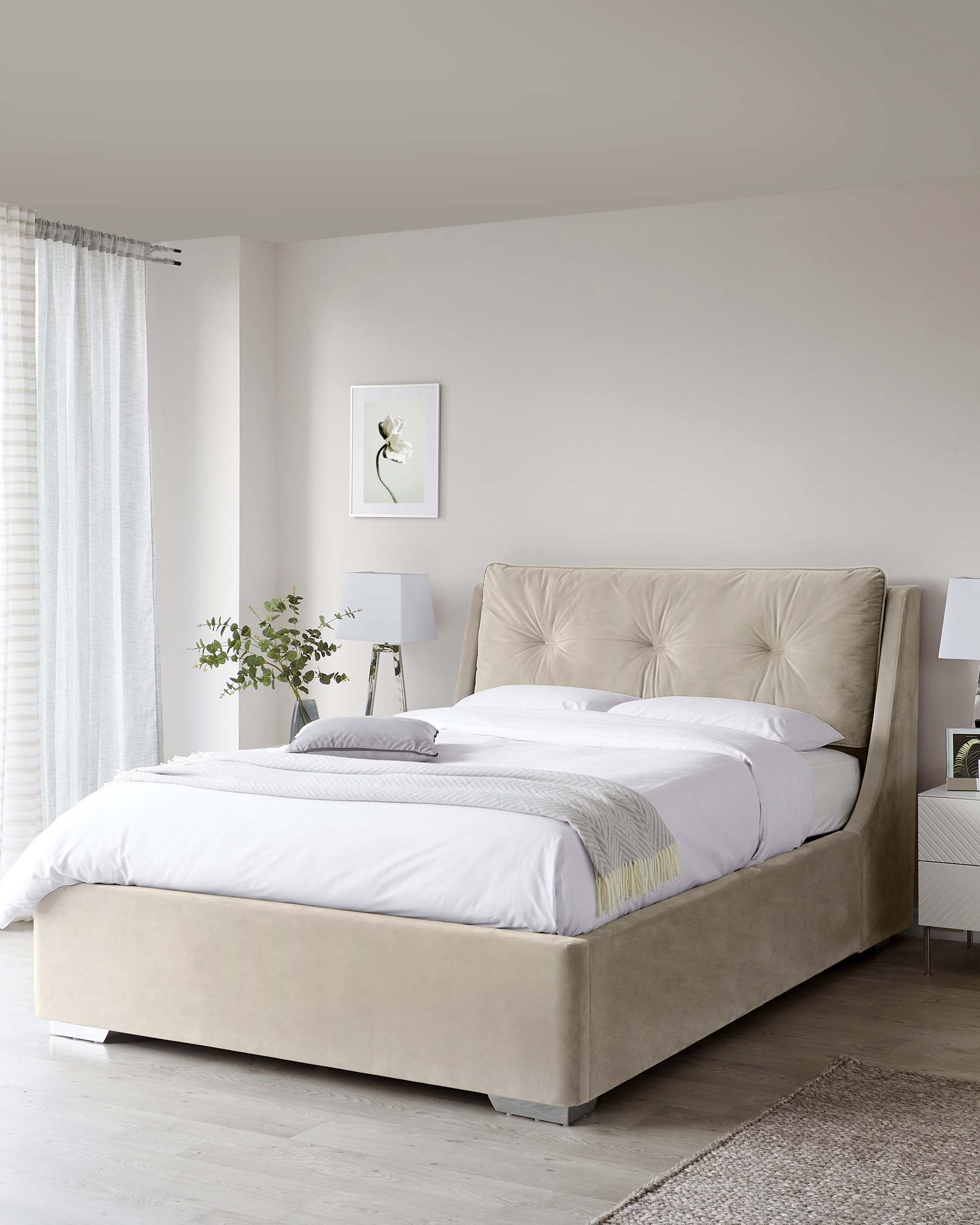 Elegant upholstered bed with a high tufted headboard in a neutral beige fabric and two small modern white bedside tables with table lamps.