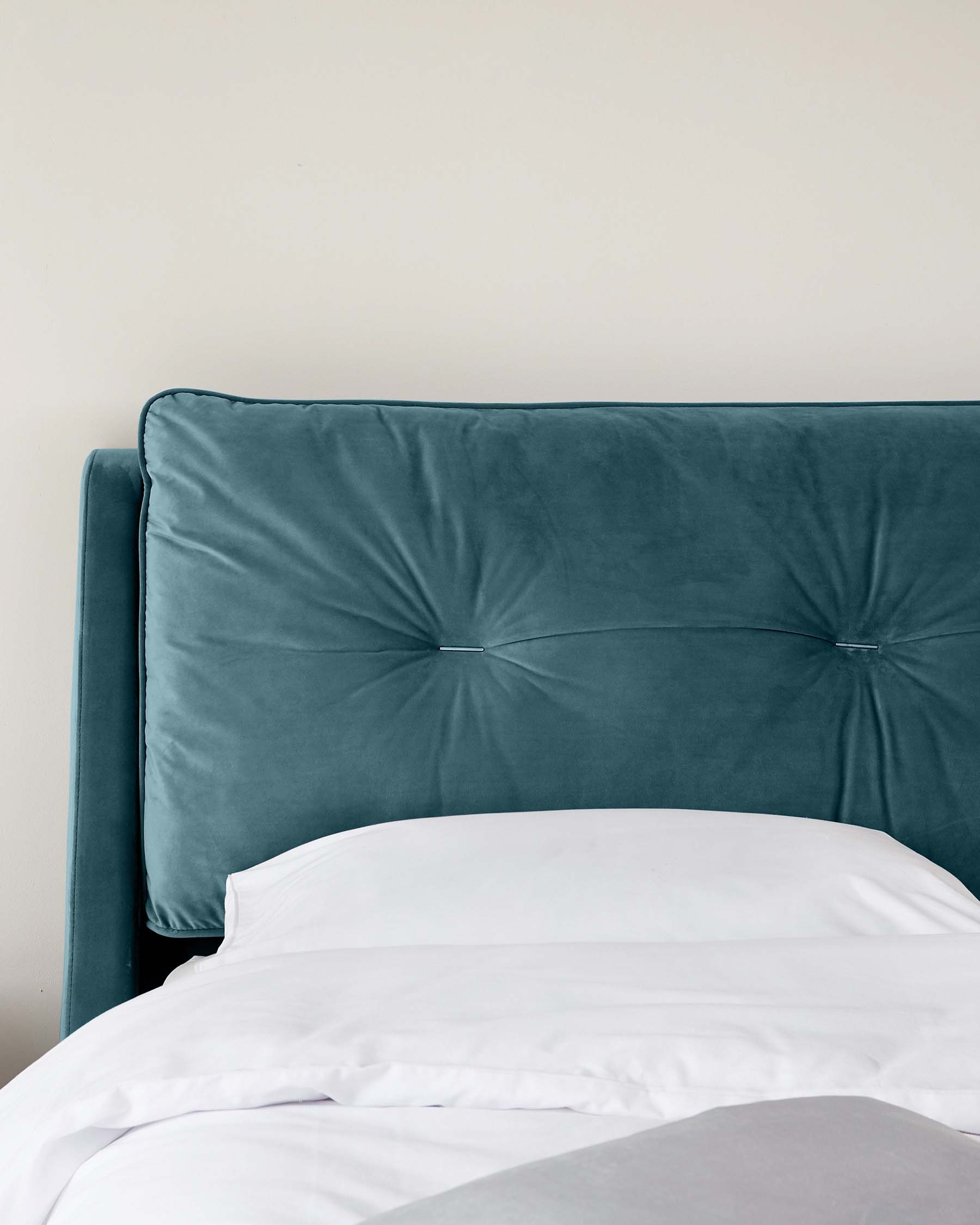 Luxurious teal upholstered headboard with tufted buttons, paired with pristine white bed linens.