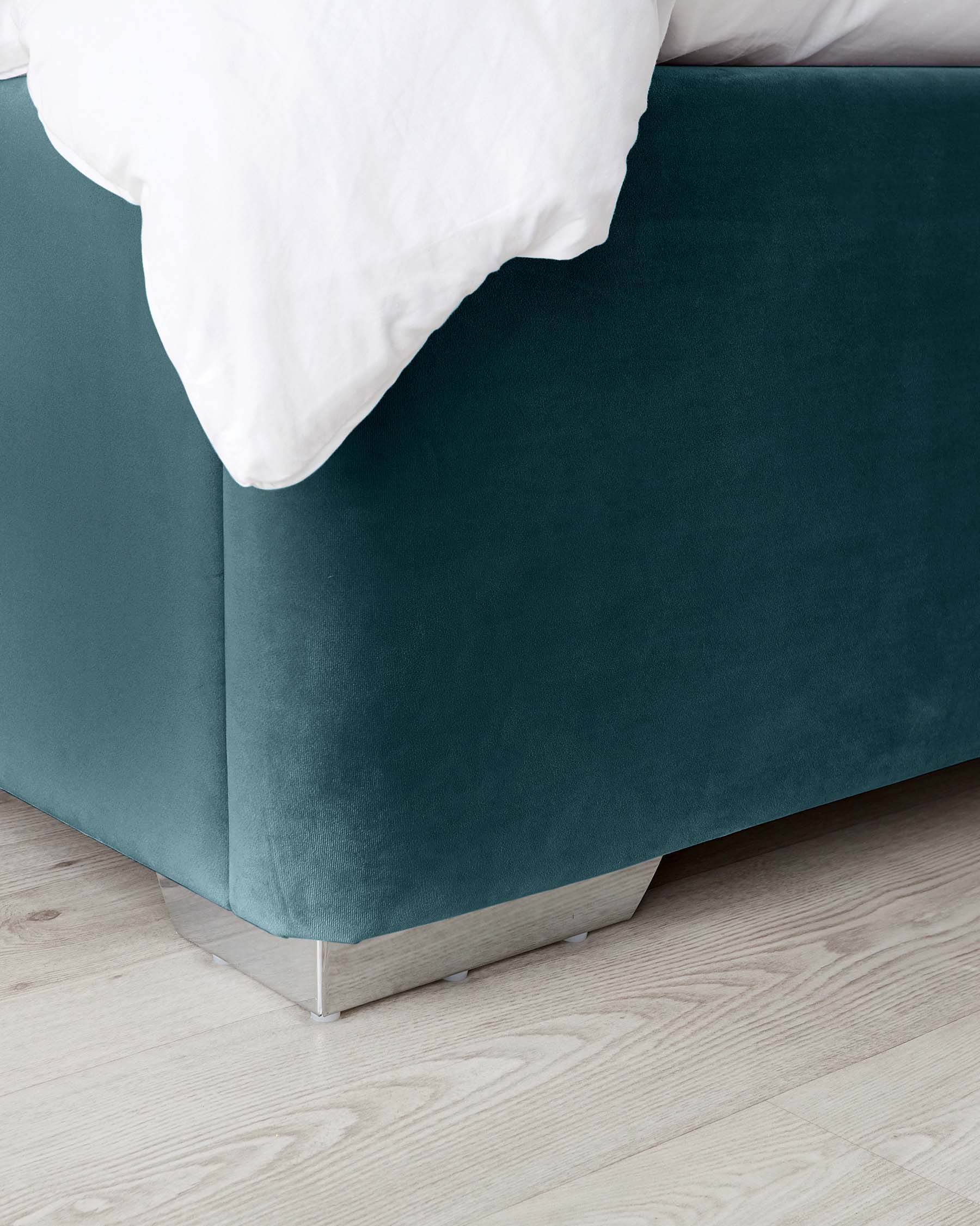 Contemporary teal upholstered bed frame with plush headboard and silver metal legs, partially covered by white bedding, on a light wood floor.