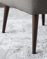 Close-up of a chair's legs showing dark wooden tapered design on a textured off-white carpet.